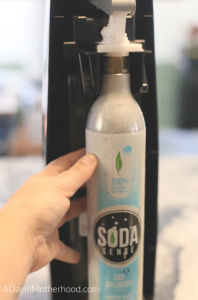 Carbinating at Home? Soda Sense Makes Your Canisters Easy to Replace = photo of canister baing attached to the sodastream machine on adayinmotherhood.com